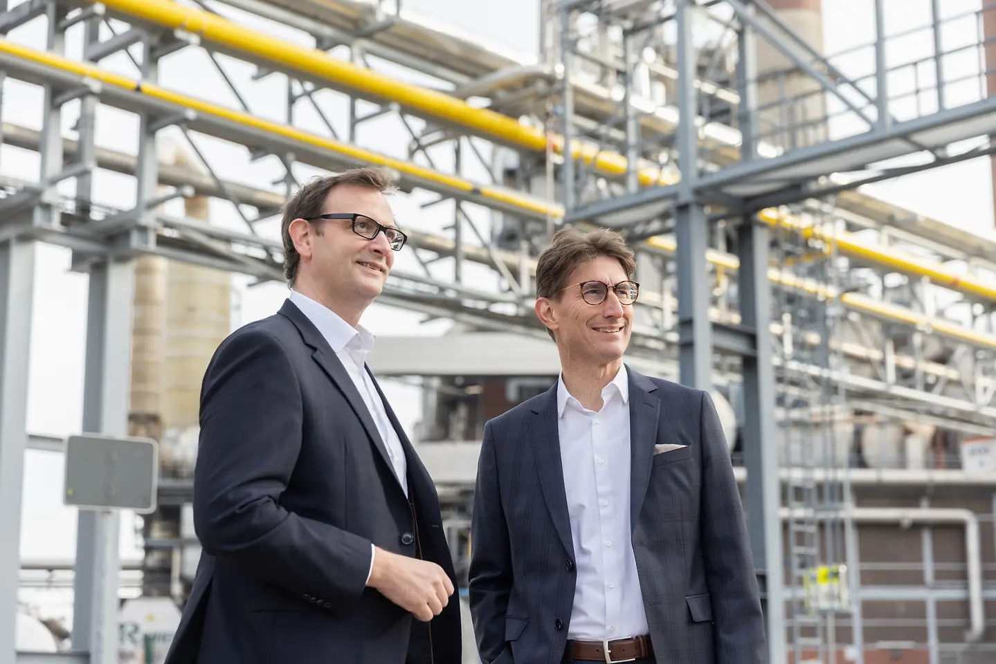 Zwei Männer in einem Industriepark stehen nebeneinander.