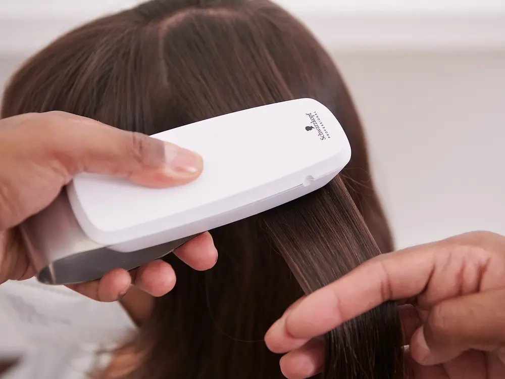 Der Friseur scannt die Haare der Kundin mit dem SalonLab Analyzer. 