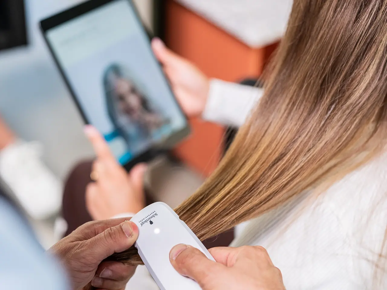 Der Friseur scannt die Haare der Kundin mit dem SalonLab Analyzer, während sie ein Tablet in der Hand hält. 