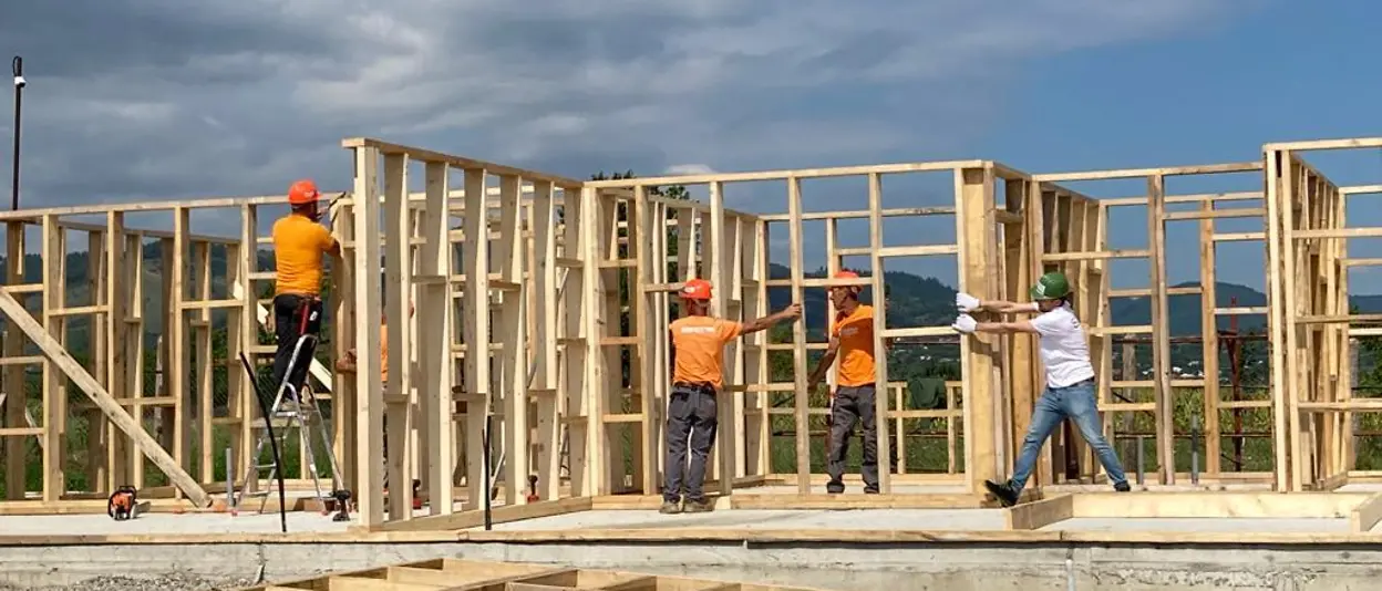 : Vier Helfer:innen arbeiten am Holzgerüst des Hauses. 