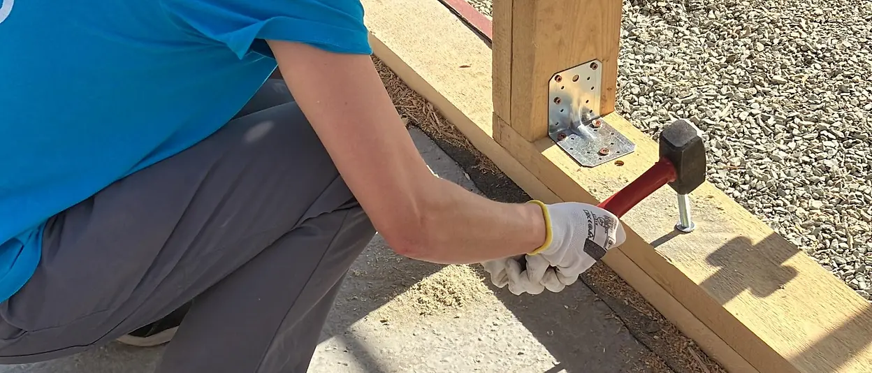 Eine Henkel-Mitarbeiterin hämmert einen Nagel ins Holzgerüst des Hauses. 