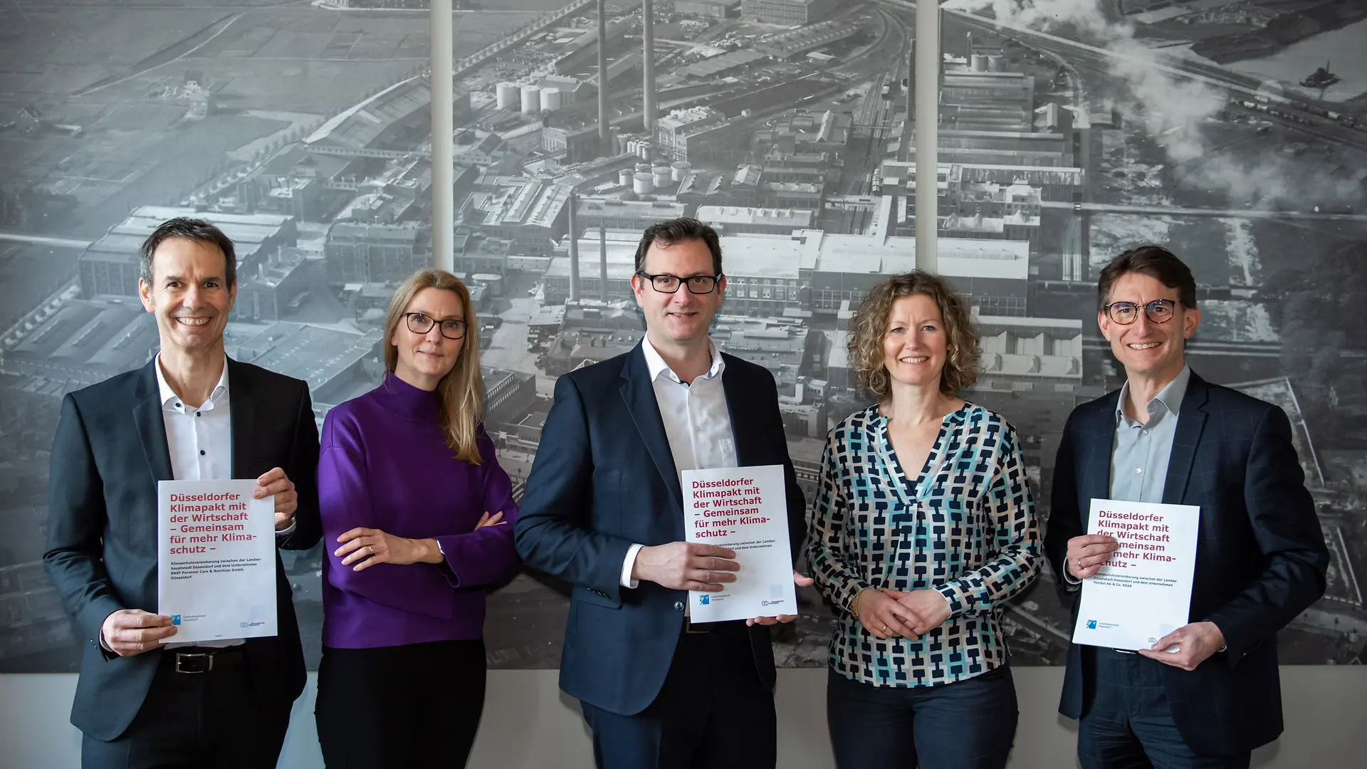 Zwei Frauen und drei Männer lächeln in die Kamera. Die Männer halten Papiere mit dem Titel des Klimapaktes.