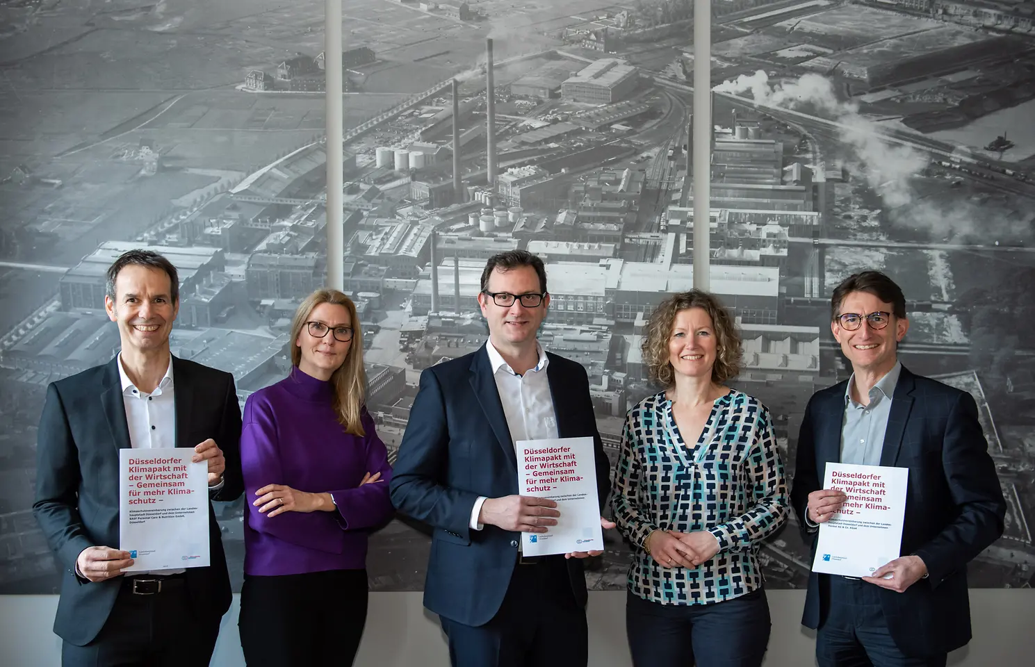 Zwei Frauen und drei Männer lächeln in die Kamera. Die Männer halten Papiere mit dem Titel des Klimapaktes.