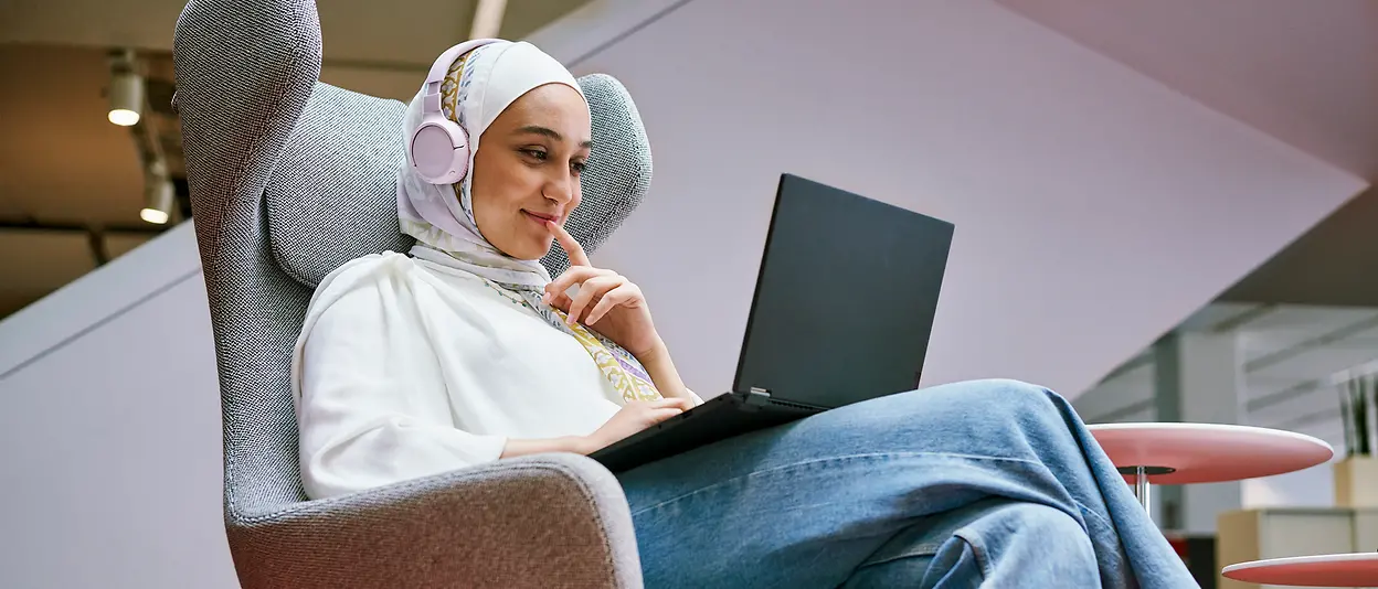 Eine Mitarbeiterin sitzt auf einem Sessel und schaut auf den Bildschirm ihres Laptops. 