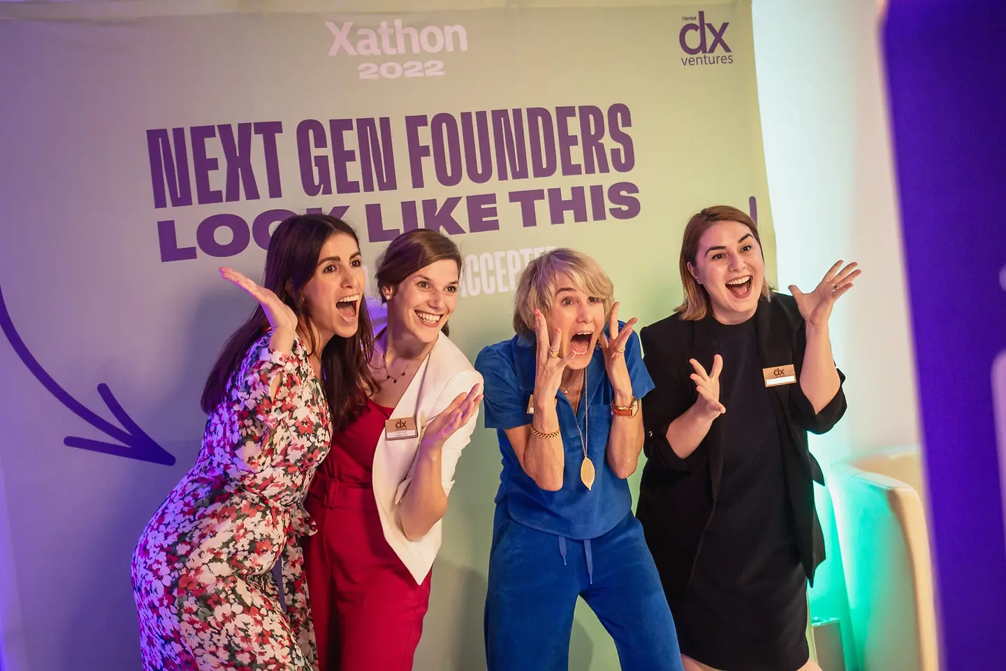 Vier Unternehmerinnen stehen vor einer Fotowand mit der Aufschrift "Next gen founders look like this". 