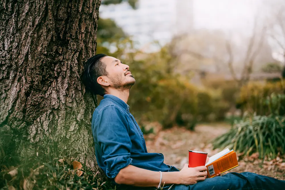 Ein Mann mit Buch lehnt an einem Baum