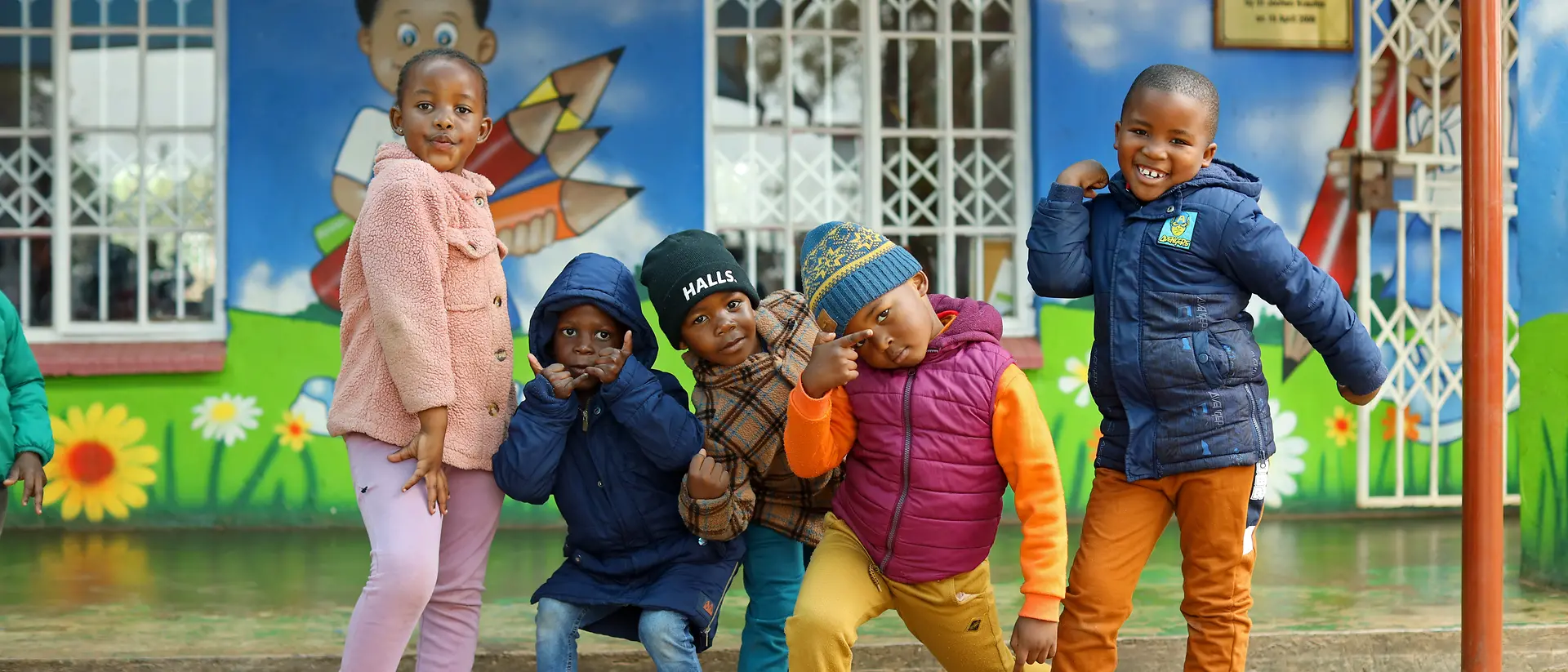 Fünf Kinder stehen in bunter Kleidung nebeneinander und machen lustige Posen.