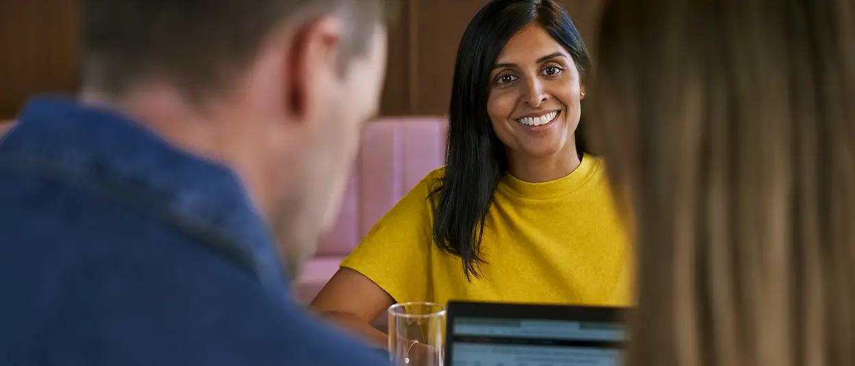 Eine Frau lächelt ihren Gegenübersitzenden im Meeting an