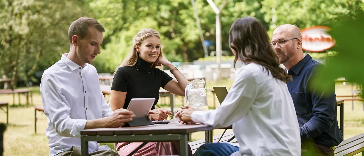 Eine Menschengruppe sitzt im Meeting draußen an einem Tisch.