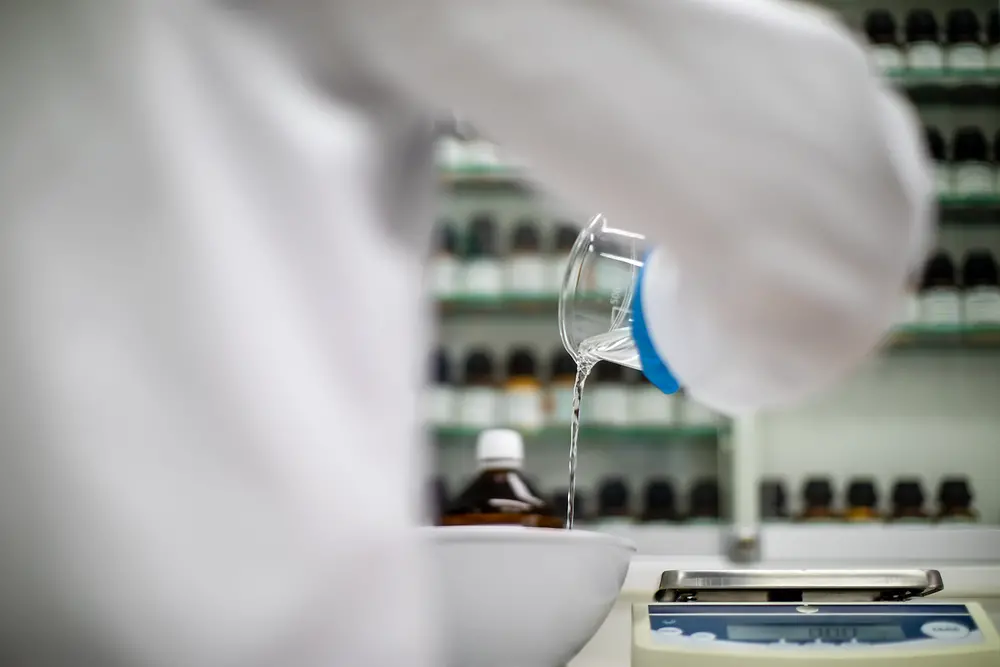 Eine Person steht im Labor und gießt eine Flüssigkeit in eine Schale. 