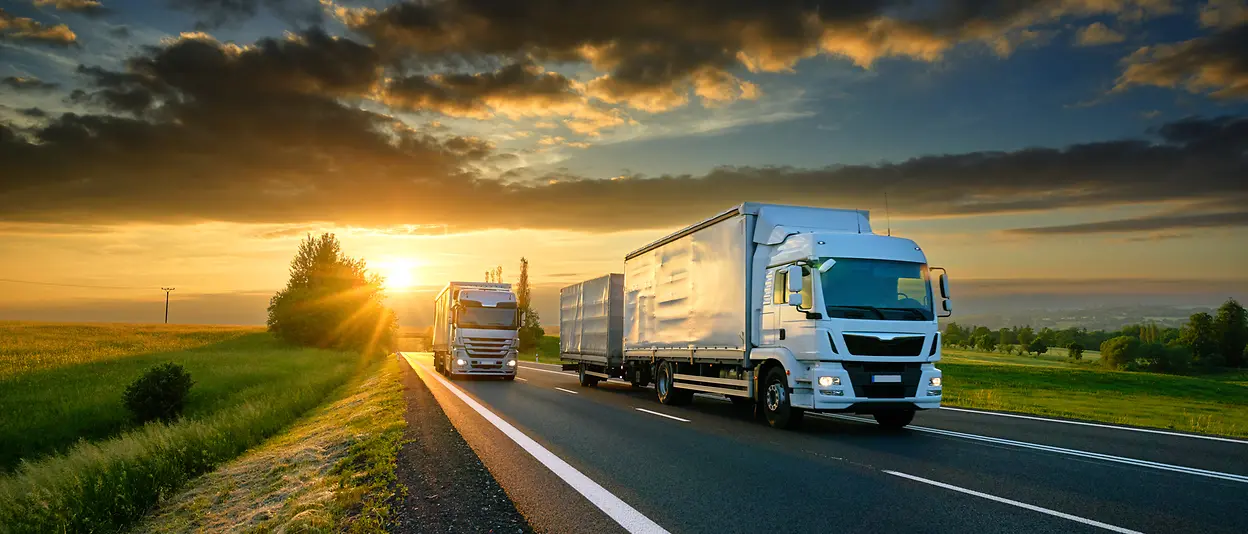 Zwei Lastwagen fahren auf einer Autobahn mit dem Sonnenuntergang im Hintergrund