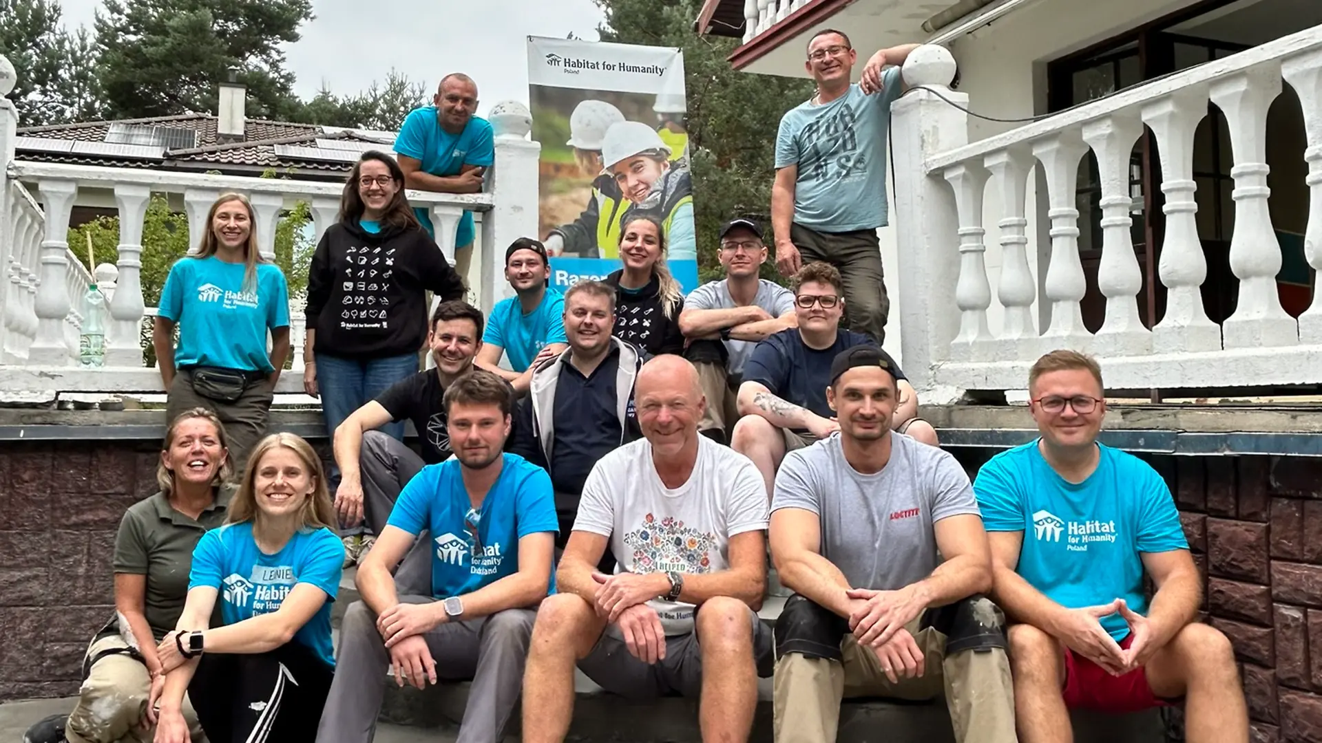 Das Baureise-Team sitzt auf einer Treppe im Garten des Hauses und lächelt in die Kamera.